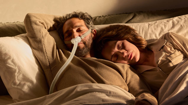 Couple in bed man wearing Resmed AirFit P10 mask